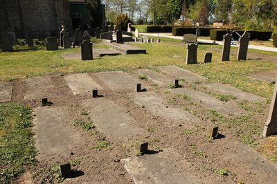 Een begraafplaats naast een kerk waarop verschillende grote blokken steen in de grond te zien zijn.