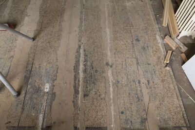 Een houten vloer waarvan delen beschilderd zijn. De beschilderde delen lijken op tapijt.
