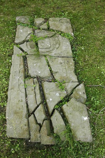 Een grafsteen ligt in stukken op een begraafplaats.