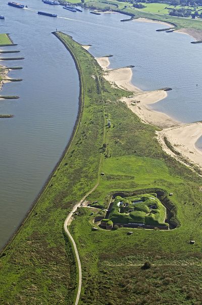 Luchtfoto van Fort Pannerdense Kop. Het stuk land steekt ver in het water. In het water zijn kirbben aangelegd.