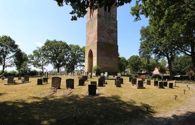 Een reeks grafmonumenten in een grasveld met op de achtergrond een toren opgetrokken uit baksteen.