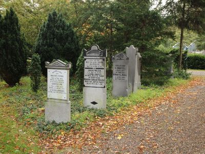 Langs een pad op een begraafplaats staan drie grafmonumenten in de berm.