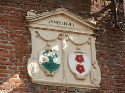 Ingezoomde foto van de wapensteen. De linkerhelft toont een groen boom en de rechterhelft twee rode rozen onder elkaar.