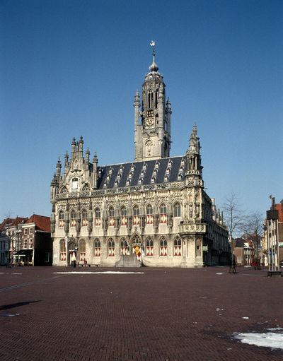 Stadshuis van Middelbrug met grote klokkentoren. Voor het gebouw een plein.