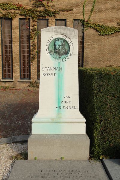 Een grafteken met een bronzen plaquette op een natuurstenen grafsteen die groen verkleurd is.