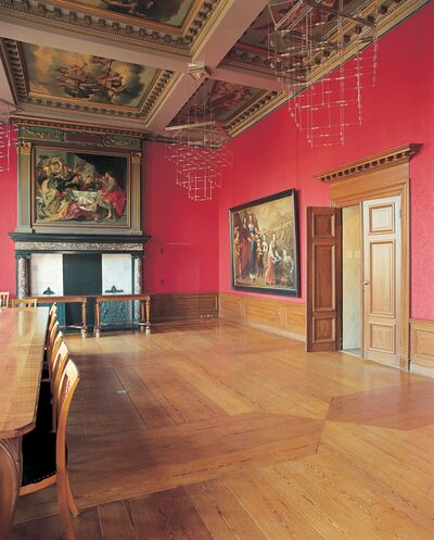 Een 17e eeuwse kamer in het Trippenhuis in Amsterdam. De kamer heeft knalrode muren en houten meubels. De houten vloer heeft een patroon.