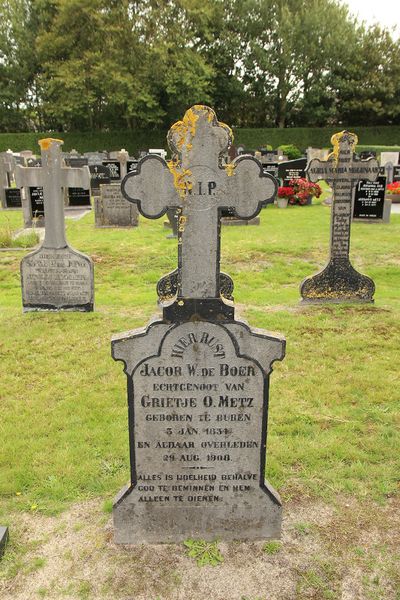 Een losstaand grafteken in het gras op een begraafplaats, bestaand uit een stèle met daarop een kruis.