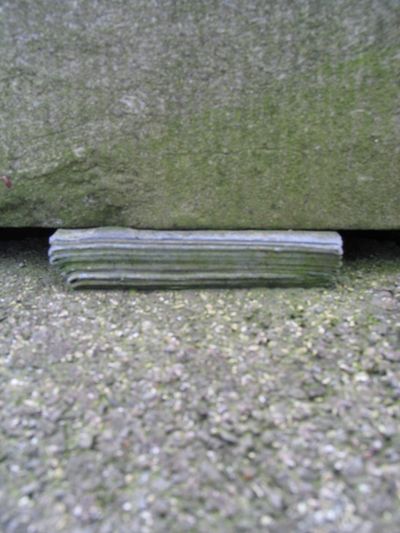 Een stukje lood ligt onder een stenen grafzerk.