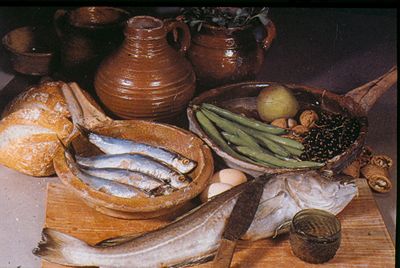 Een schilderij met potten en schalen met daarin onder andere vis en bonen.