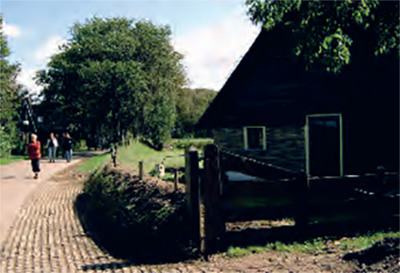 Tuinwal met aan de linkerkant een weg met voetgangers en aan de rechterkant een boerderij.