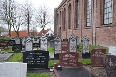 Een kerkhof met veel dezelfde grafstenen in zwart of rood graniet, naast een rode bakstenen kerk.