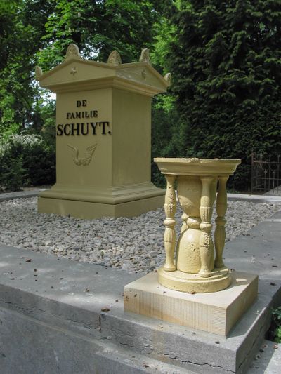 Een witte gietijzeren zandloper staat op een pedestal op een begraafplaats.