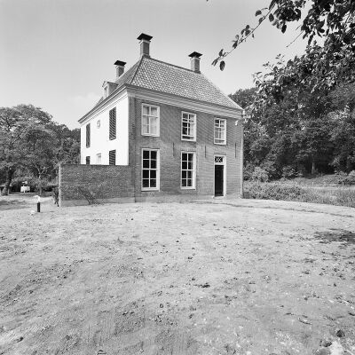 Zwart-wit foto van het vooraanzicht van Huis Appeltern. Er ligt een groot grasveld voor het huis en aan de linkerkant staat een aangebouwde muur waarachter een tuin ligt. Rechts loopt een watertje.