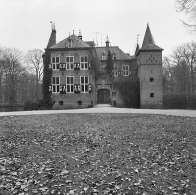 Zwart-witfoto van het kasteel en de oprit. Het gebouw is deels begroeid met klimop. In de achtergrond is een gracht te zien en een bos met kale bomen.