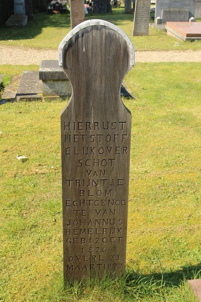 Een staand grafmonument van hout met tekst en een zinken kapje bovenop, staand in een gazon