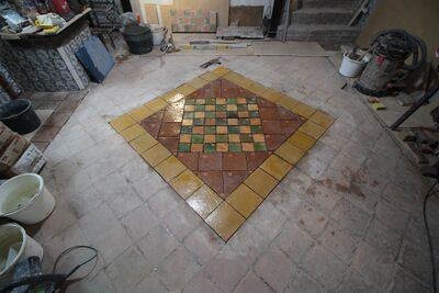 Estrikenvloer tijdens het vervangingsproces. Het patroon bestaat uit oker, terra, groene en oranje kleurige tegels.