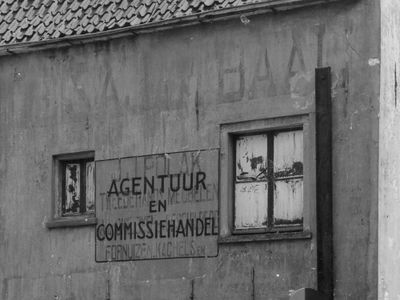 Zwartwit foto van het pand aan Klooster 21-23, met op de gevel een vervaagde tekst "De Sajetbaal" en een gevelreclame "Agentuur en commissiehandel"