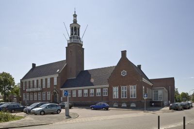 Raadhuis Hoogeveen met klokkentoren. In de voorgrond geparkeerde auto’s en parkeerautomaat.