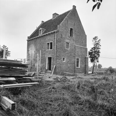 Zwart-witfoto van de Wezenhorst. Links liggen houten balken en planken in de wildgroei. Rechts van het huis staat een jong boompje.