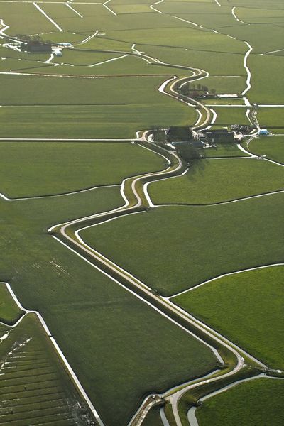 Luchtfoto van de Slagtedijk. Weiland waar wegen en sloten doorheen lopen. In het midden van de foto is een boerderij te zien.