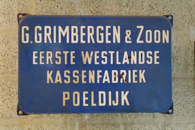 Blauw ijzeren kassenschild waar met witte letters o.a. kassenfabriek Poeldijk op staat.