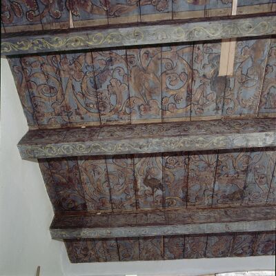 De onderkant van een houten vloer. De planken zijn donker en hebben een decoratieve beschildering.
