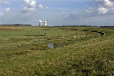 Foto van een polder met in de achtergrond twee torens waar rook uit komt.