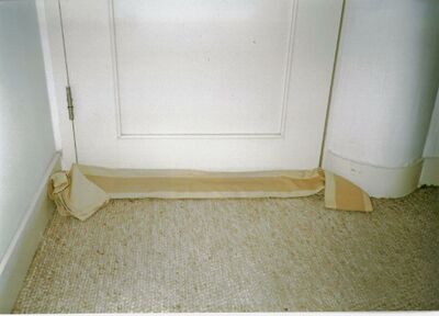 afbeelding van een houten binnendeur met op de grond een gerolde lap stof om tocht tegen te houden