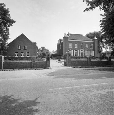Zwart-witfoto van een weg met twee grote huizen achter een openstaand hek, met een oprijlaan die tussen de twee huizen ligt.