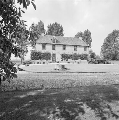 zwart-witfoto van de voorgevel van het huis met tuin in de voorgrond. Achter het huis staat een reeks bomen.