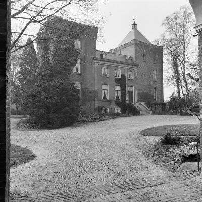 Zwart-witfoto van de voorgevel van het kasteel, met een pad in de voorgrond dat om het gebouw heen loopt. De linker toren is overgroeid met klimop. In de achtergrond staan kale bomen.