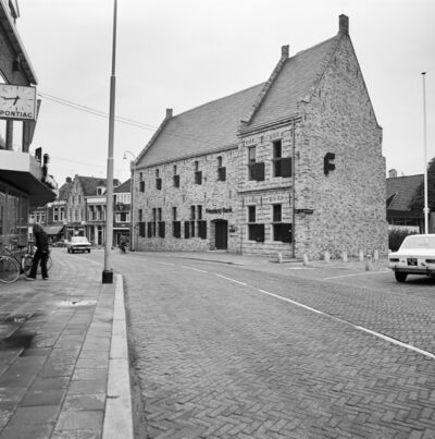 Zwart-witfoto van een straat die naar links buigt met een middeleeuws gebouw.