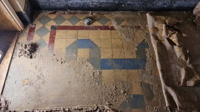 Patroontegelvloer met gele, blauwe, groene en rode vierkante tegels. De vloer is half zichtbaar vanwege de andere vloersoort die er nog overheen ligt.