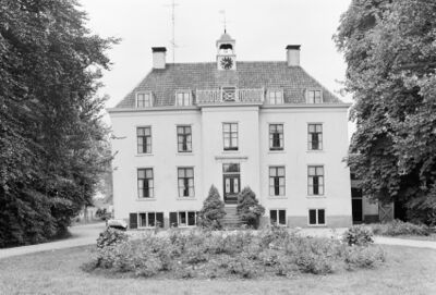 Zwart-wit foto van Huis Teisterbant. In de voorgrond staat een stekje met bloemen. Er is een oprijlaan van grind. De deur is te bereiken via een stenen buitentrap.