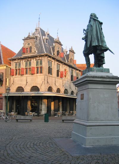 Standbeeld van Jan Pieterszoon Coen in Hoorn. Hij staat op een voetstuk met één been naar voren in het midden van een plein. Aan de randen van het plein bevinden zich winkels en cafés.