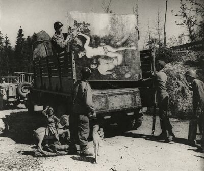 Zwartwit foto van een aantal soldaten met een vrachtwagen met daarop een groot schilderij